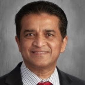 Smiling person in a suit and tie against a gray background.